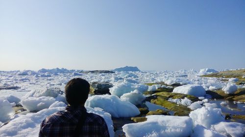 Rear view of man standing in front of icebergs against clear sky