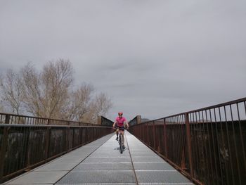 Rear view of woman walking on footbridge against sky