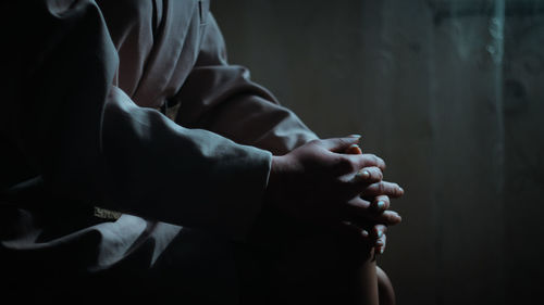 Midsection of woman with hands clasped sitting at home