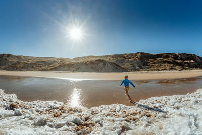 View from ocean of young child running from waves on a sunny day in new zealand