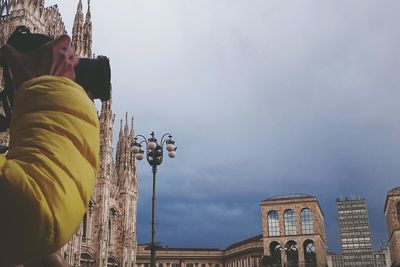 Cropped image of photographer photographing by duomo di milano against cloudy sky