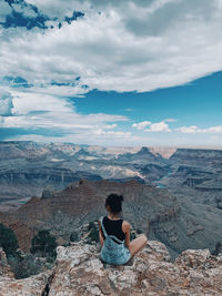 Rear view of woman sitting on rock against sky