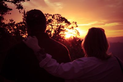 Rear view of man and woman standing against sky during sunset
