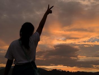 Silhouette woman with arms raised against sky during sunset