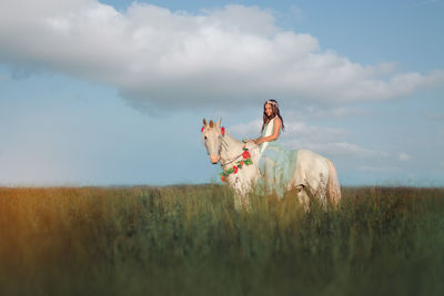 Girl riding horse on field against sky