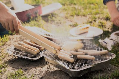 Cropped hand preparing sausages on barbecue grill