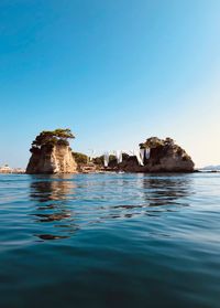 View of rock in sea against clear blue sky