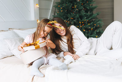 Cute funny little girl with mother on bed in room with christmas tree