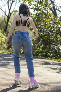 Brunette woman from behind skating in the park with pink roller skates