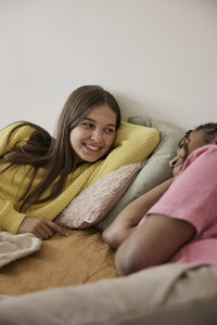Smiling teenage girl talking with female friend while lying in bedroom