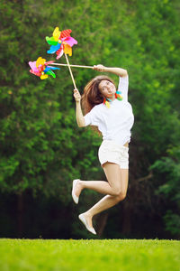 Portrait of beautiful smiling woman holding pinwheel toys while jumping on field
