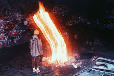 Rear view of woman standing by bonfire in graffiti cave