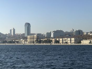 Sea by buildings against clear sky