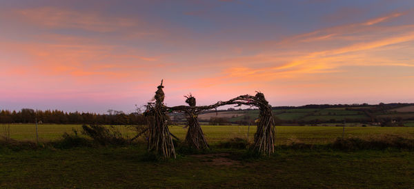 Wicker witches on field against sky during sunset