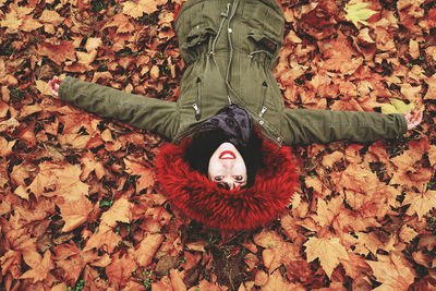 High angle portrait of woman lying amidst autumn leaves on field