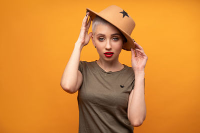 Close-up portrait of young woman wearing hat against orange background