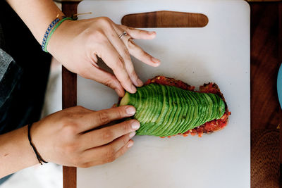 From above crop cook preparing sandwich and stacking sliced avocado on bread on white stand