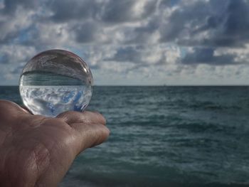 Close-up of hand holding crystal ball against sea