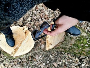 Low section of man holding sunglasses while standing on logs