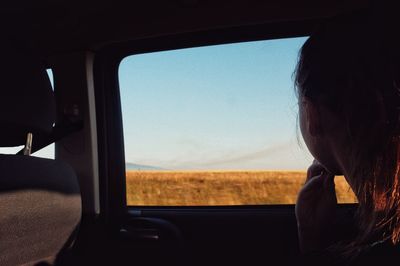Young woman looking at landscape through car window 