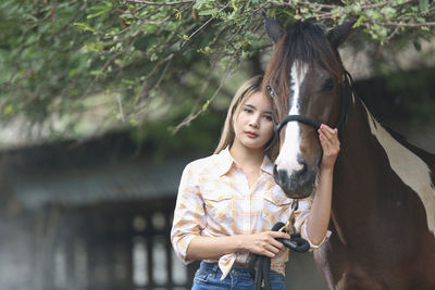 Portrait of young woman standing by horse