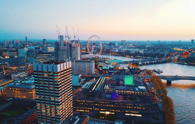 Aerial view of river amidst illuminated city against sky during sunset