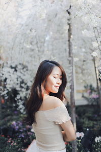 Young woman smiling while standing against white flowering trees at park