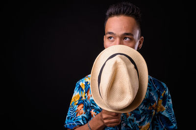 Portrait of man holding hat against black background