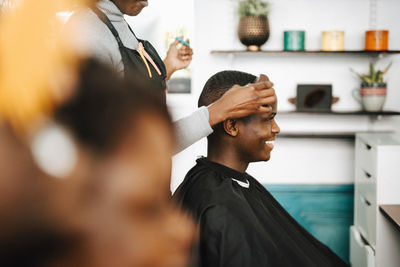 Midsection of female hairdresser cutting hair of smiling male customer in barber shop