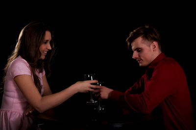 Side view of young couple toasting wineglasses against black background