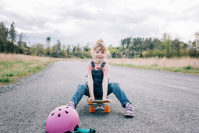 Portrait of a young girl sat on a skateboard smiling