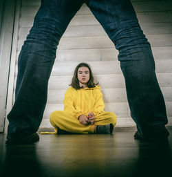 Portrait of girl sitting on floor while man standing in foreground