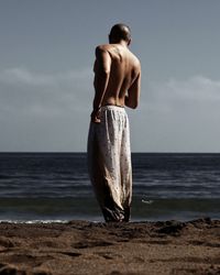 Rear view of shirtless man standing on beach