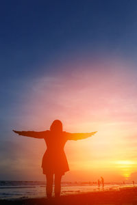 Rear view of silhouette man standing on beach against sky during sunset