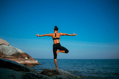 Full length of woman doing yoga on rock against sea