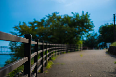 Footpath by fence against blue sky