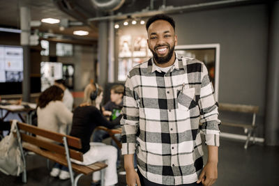 Portrait of happy male teacher wearing plaid shirt while standing in high school