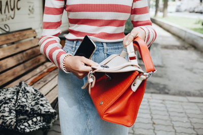 Midsection of woman holding purse on footpath