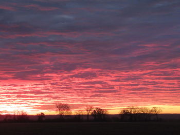 Silhouette trees on field against dramatic sky during sunset