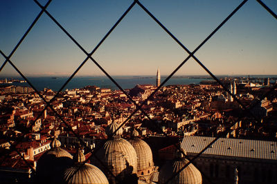 Cityscape against sky seen through chainlink fence