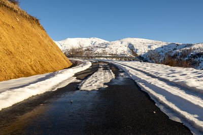 Road amidst snowcapped mountains against clear sky