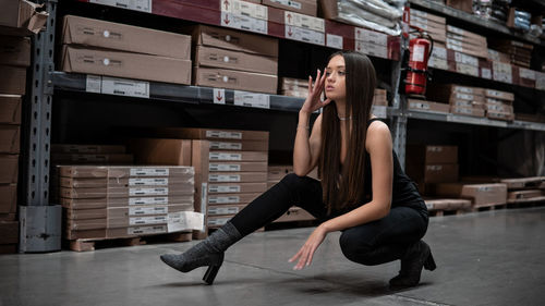 Full length of young woman stretching on floor in warehouse