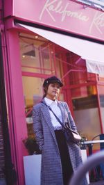 Portrait of young woman standing against store