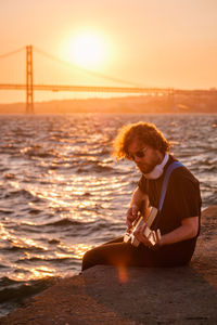 Portrait of young woman sitting on pier at sunset