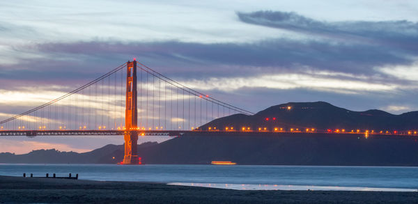 Suspension bridge over sea against cloudy sky