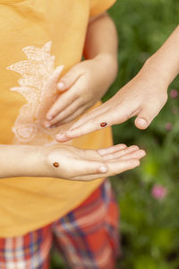 Midsection of girl with ladybugs on hand standing outdoors