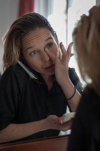 Reflection of woman applying powder compact while talking on phone on mirror