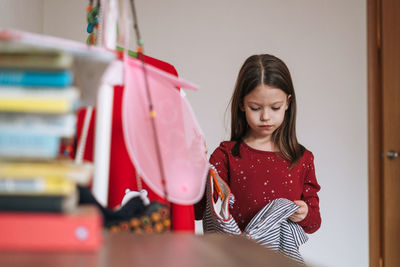 Thinking girl with long dark hair in red dress among her beautiful dresses in wardrobe at home