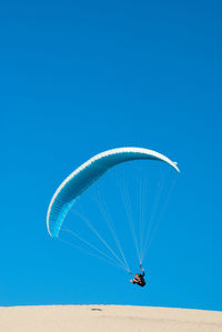 Low angle view of paragliding against clear blue sky