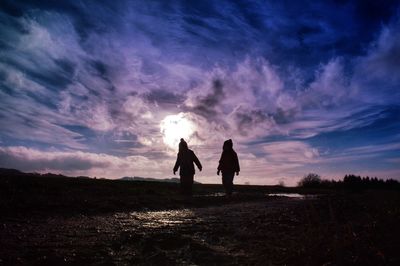 Silhouette sibling on field against sky during sunset